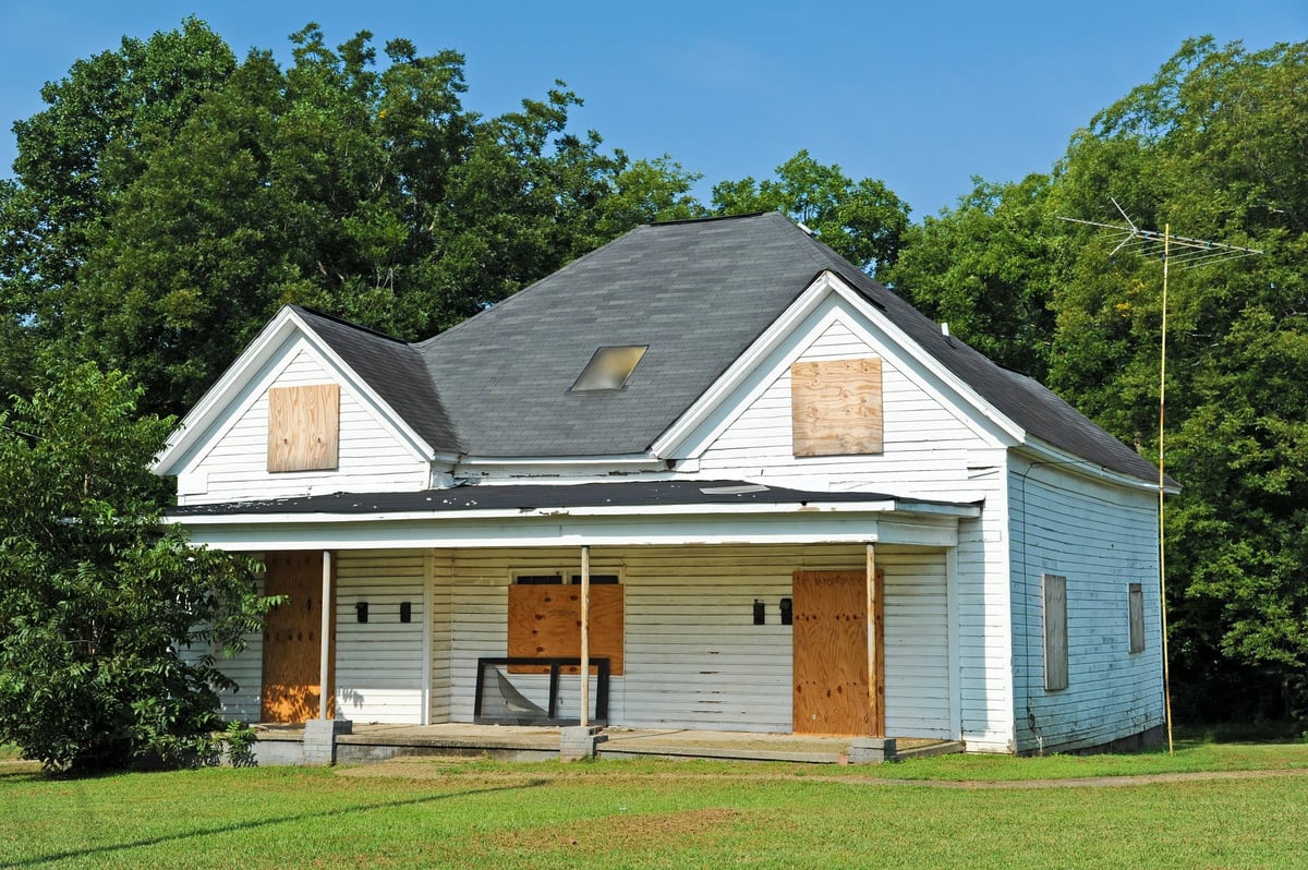 Distressed abandoned house with boarded up windows — we buy homes in any condition